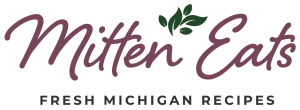 Mitten Eats logo. Purple script lettering and a green sprig of leaves above the words.
