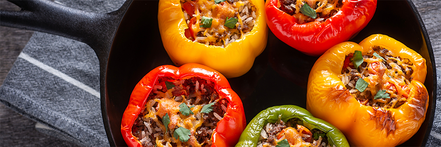 Wide shot of a yellow, red, and green peppers filled with rice, meat and cheese. Peppers are displayed in a black cast iron skillet.