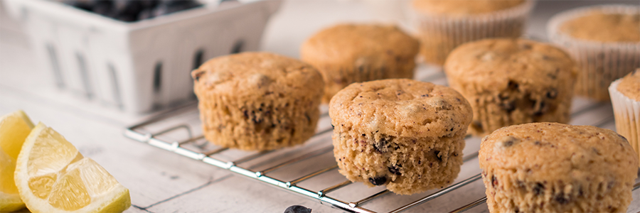 close up of muffins on a cooling rack. A pint of fresh blueberries is blurred in the background.