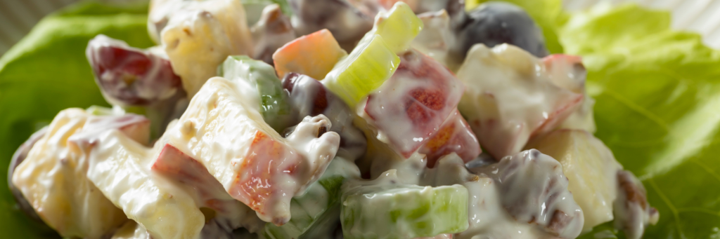 Close up shot of salad with apples, nuts, and celery in a creamy dressing. Salad is resting on a bed of lettuce.