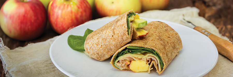 Wide shot of a plate displaying a tortilla filled with turkey, spinach, apples, and cheese.