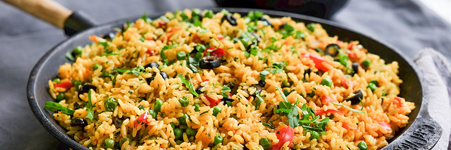 Wide shot of a skillet with rice medley with tomatoes, peppers, peas, and onions.
