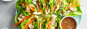 asian-lettuce-wraps Close up of lettuce with chicken, carrots, and onions wrapped together with a side dipping sauce.