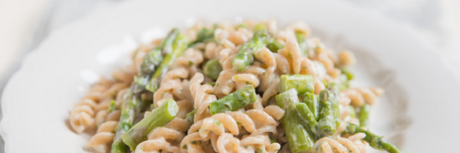 Close up of whole-grain fusilli pasta and asparagus coated in Parmesan sauce on a white plate.