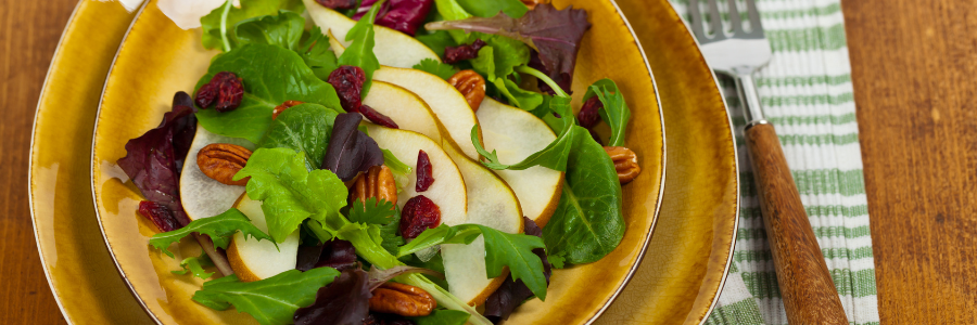 Green salad with pears, walnuts, and dried cranberries on dark yellow plate.