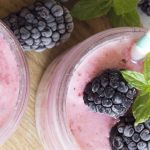 Close up shot of two glasses filled with pink-hued smoothies topped with frozen black berries.