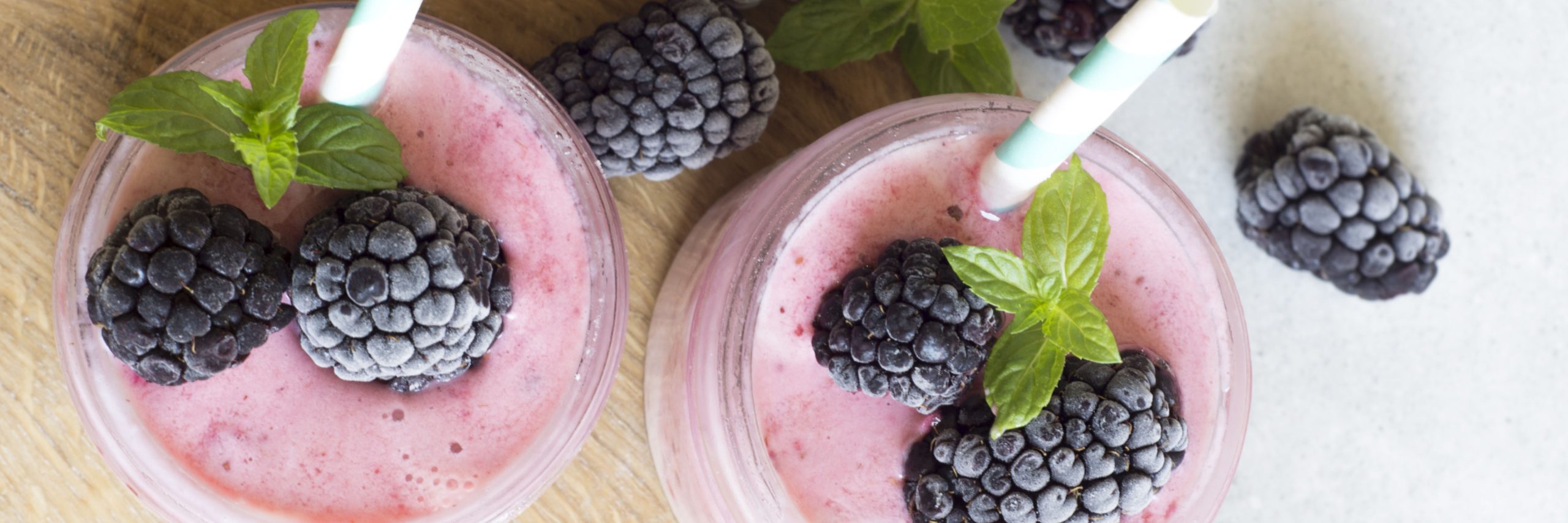 Close up shot of two glasses filled with pink-hued smoothies topped with frozen black berries.