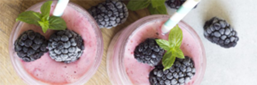 Clear glass full of banana berry smoothie topped with blackberries.