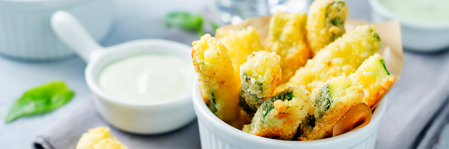 Close shot of zucchini-shaped fries that have been coated in breadcrumbs and Parmesan cheese. Fries are displayed in a white ramekin.