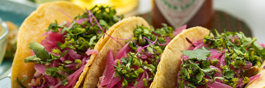 Close up of three corn tortilla tacos filled generously with chicken, cilantro, and red onions displayed on a blue platter.