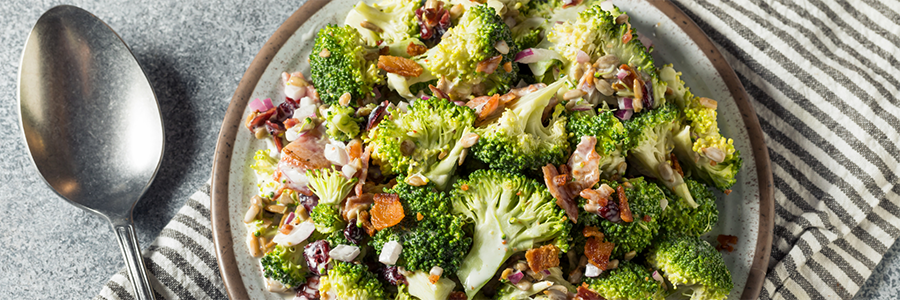 Close up of a bowl of salad with broccoli, sunflower seeds, red onion, and bacon bits.