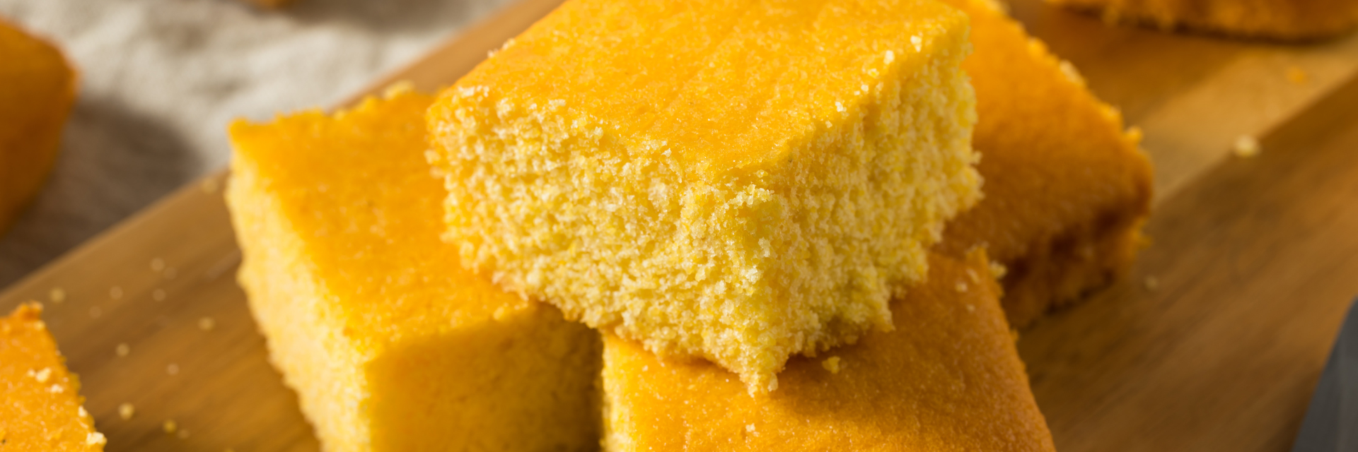 Four squares of golden cornbread stacked on each other on a wood cutting board.