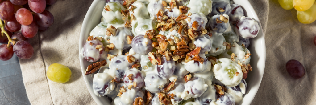 Aerial view of grapes covered in yogurt with nuts sprinkled on the top in a while bowl on top of white linen.