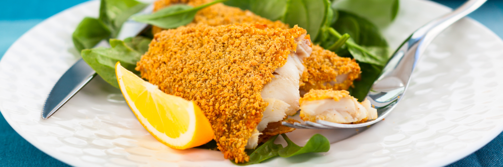 Shot of crispy breaded fish fillets on a bed of fresh spinach and garnished with a lemon wedge.