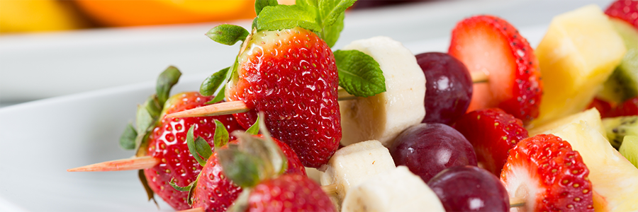 Close up of fruit on skewers including strawberries, bananas, and grapes.