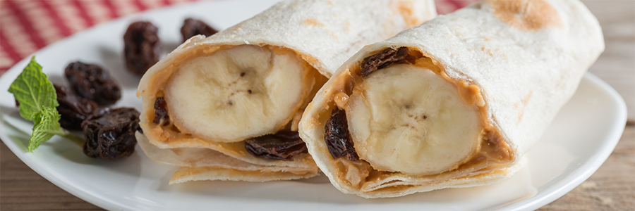Close up of a banana wrapped in a tortilla with peanut butter and raisins.
