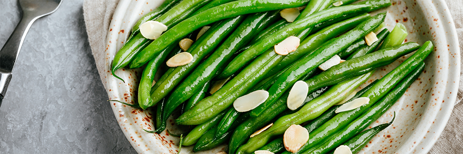 Close up of green beans garnished with sliced almonds. Displayed on a stoneware platter.