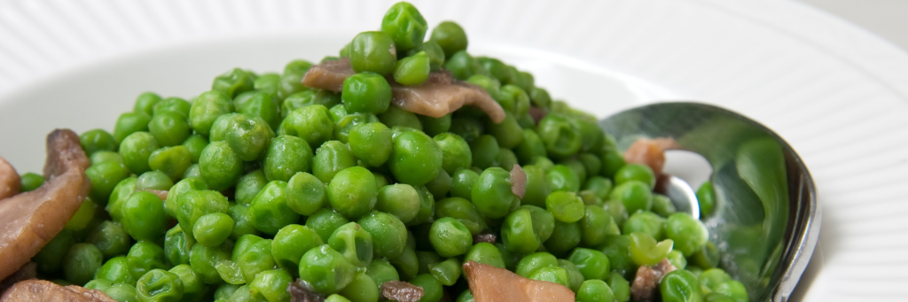 Close up shot of green peas and cremini mushrooms on a white platter.