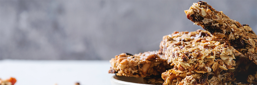 Wide shot of stacked breakfast bars made with oats, coconut, and raisins displayed in a stoneware bowl.