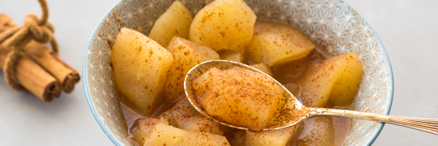 Close up of cooked apple chunks with cinnamon with a gold spoon in a gray stone bowl.
