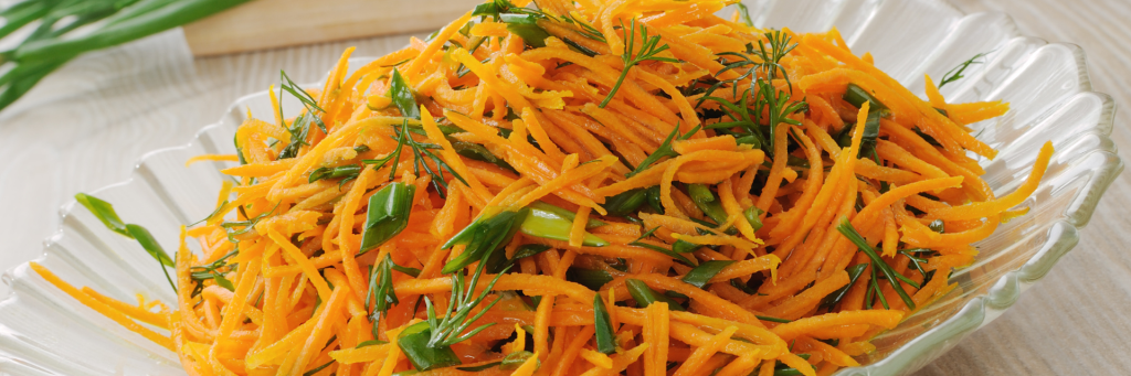 Close up shot of shredded carrots on a platter. Shredded carrots are garnished with parsley and green onion.