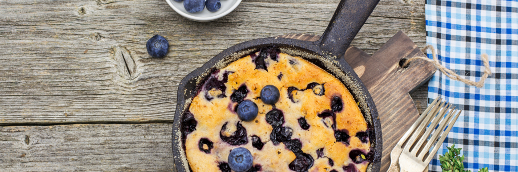 Wide shot of a cast iron skilled with a baked blueberry pancake. Pancake is garnished with blueberries.