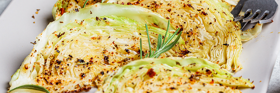 Close up shot of three roasted cabbage wedges on a platter. Garnished with spices and herbs.