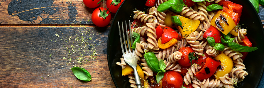 Close up of a plate with whole wheat rotini pasta, fresh cherry tomatoes and basil, and grilled peppers.