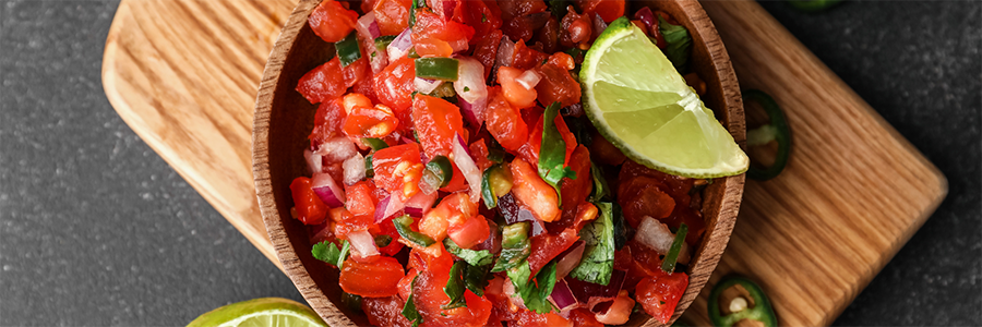 Close up of fresh salsa with tomatoes, red onion, jalapeno, and cilantro. Garnished with a lime wedge.