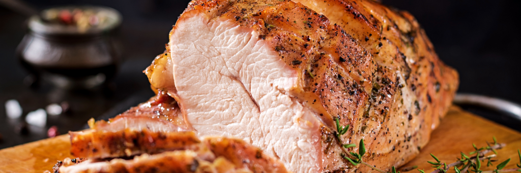 Close up of perfectly seasoned and juicy roast turkey on a cutting board with a black background.