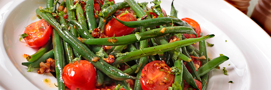 Close up of sautéed fresh green beans and cherry tomatoes displayed on a white platter.