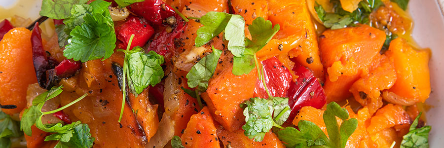 Close up of cubed sweet potatoes with red peppers and spices. Garnished with parsley.