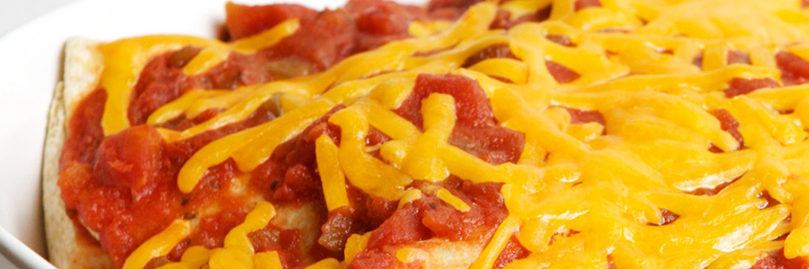 Close up view of whole-wheat tortillas topped with salsa and shredded cheddar cheese in a white casserole dish.