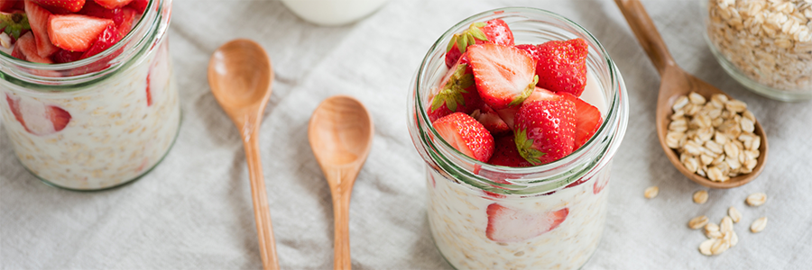 Close up skewed shot of a small white bowl containing oatmeal topped with yogurt and strawberries.
