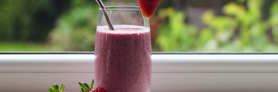 Strawberry smoothie in a clear glass with a straw and strawberries for garnish