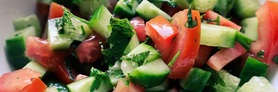 Close up view of salad with chopped cucumbers, tomatoes, onions, and herbs