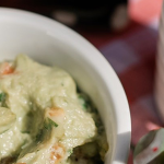 Salsa dip in a white bowl and a small bowl holding carrot and celery sticks sitting on a red checked tablecloth. The bowls are placed next to a small succulent plant.