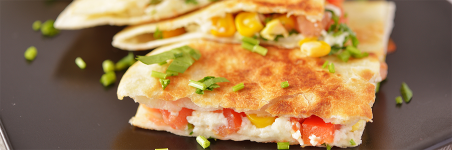 Close up shot of quartered tortillas filled with tomatoes, corn, and cheese. Garnished with green onion and cilantro.