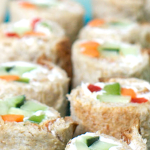 Close up view of a nine pieces of vegetable sushi filled with peppers and cream cheese on a long plate with chop sticks resting on the edge.