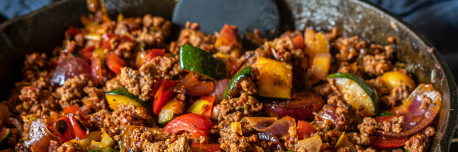 Close up on black skillet full of ground turkey, zucchini, red and yellow bell peppers, and onion.
