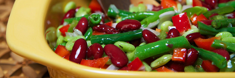 Shot of a salad with green beans, red kidney beans, edamame, and red peppers in a yellow platter.