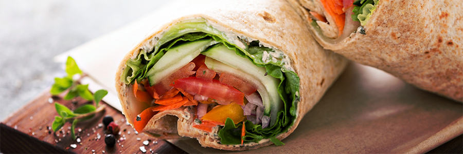 Close up of a whole-wheat tortilla filled with tomato, cucumber, lettuce, and shredded carrot.