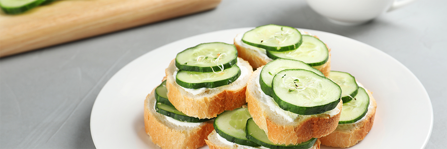 Close up shot of slices of French baguette stacked and topped with cream cheese and cucumber slices.