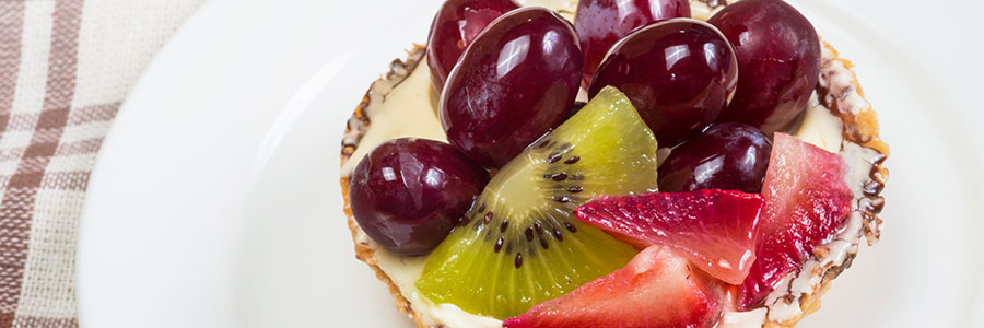 Close up of an English muffing topped with cream cheese, grapes, sliced strawberries and kiwi.