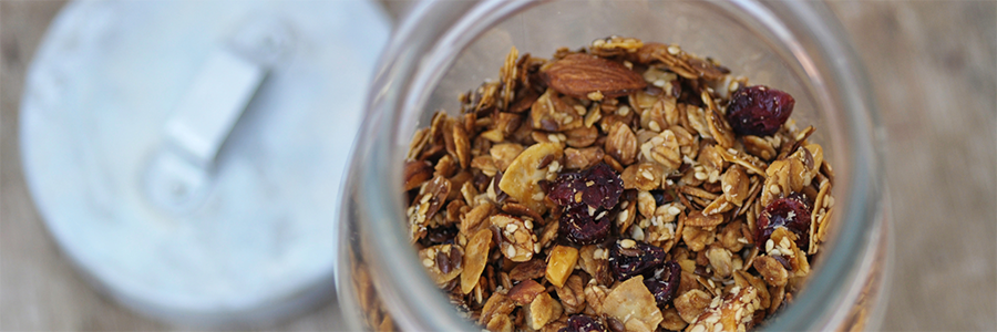 Close up of a jar filled with granola with oats, almonds, cherries, and raisins.
