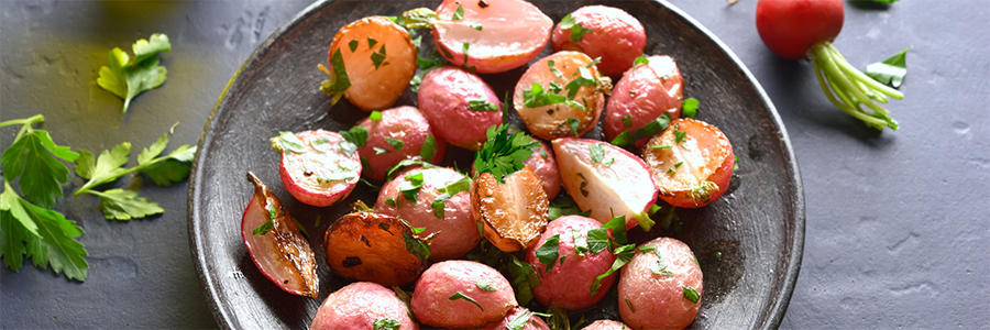 Wide shot of roasted halved radishes garnished with parsley and plated on a dark stoneware platter