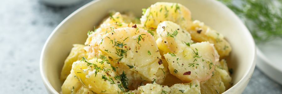 Leanne Brown's Ever Popular Potato Salad in a white bowl and green garnish on top.