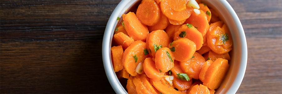 Close up of a bowl of sliced glazed sliced carrots garnished with parsley flakes.
