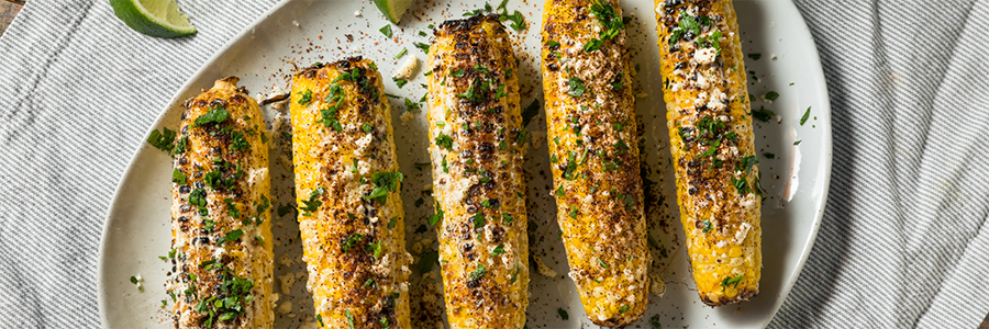 Wide shot of a platter with Mexican street corn, broiled and topped with cotija cheese and crema.