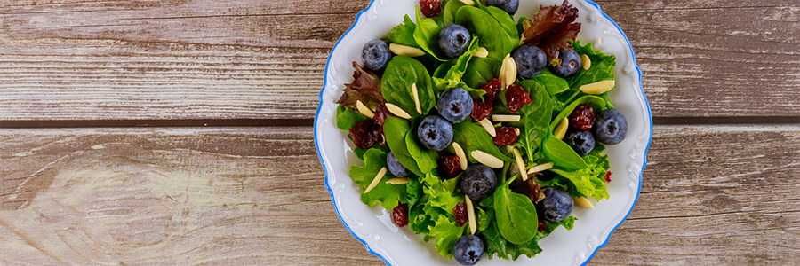 Close up of a mixed greens salad with fresh blueberries, dried cranberries, and almonds.